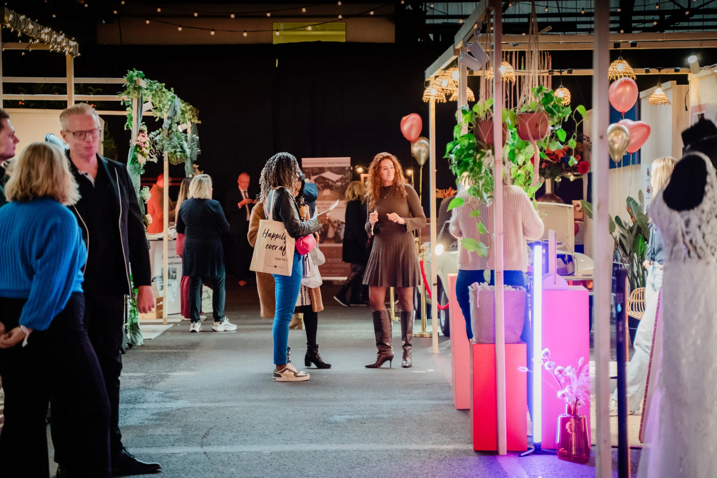 Bezoekers in gesprek tussen stands met hangplanten en roze ballonnen
